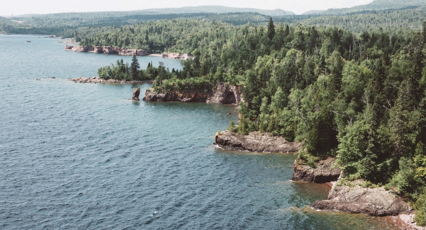 The rocky and tree-lined shore of Lake Superior frames the blue water of the lake. 
